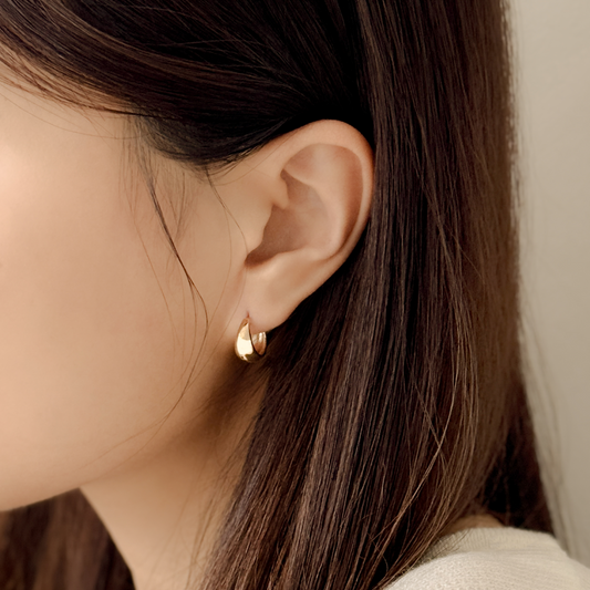Close-up of an ear wearing a gold earring with brown hair and beige background