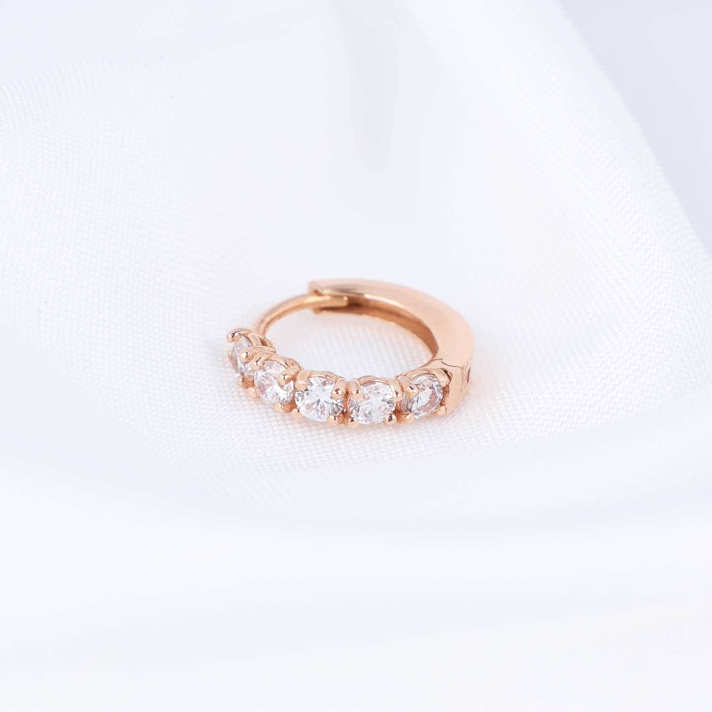 Rose gold huggie hoop earring with clear stones on a light gray background