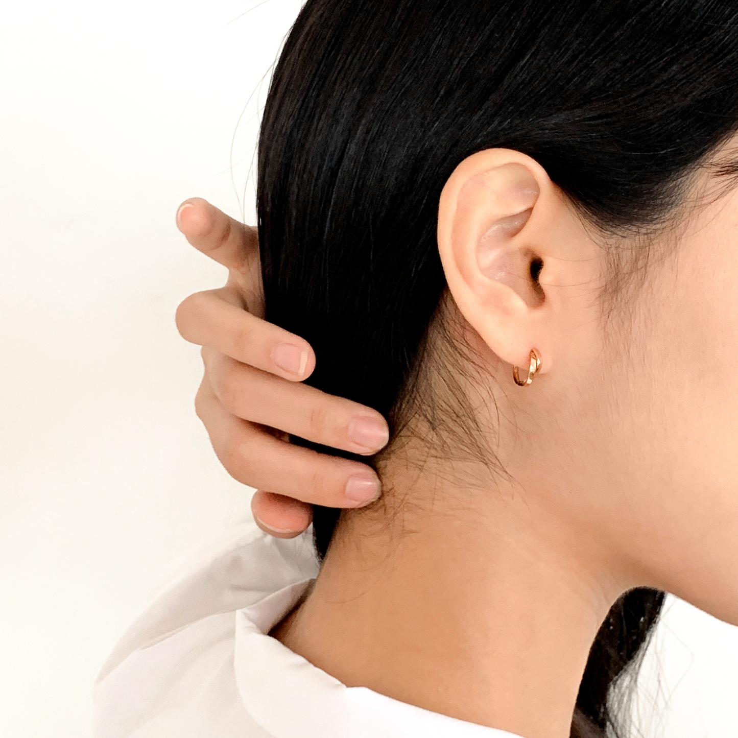 Close-up of a person wearing a gold hoop earring with a plain background