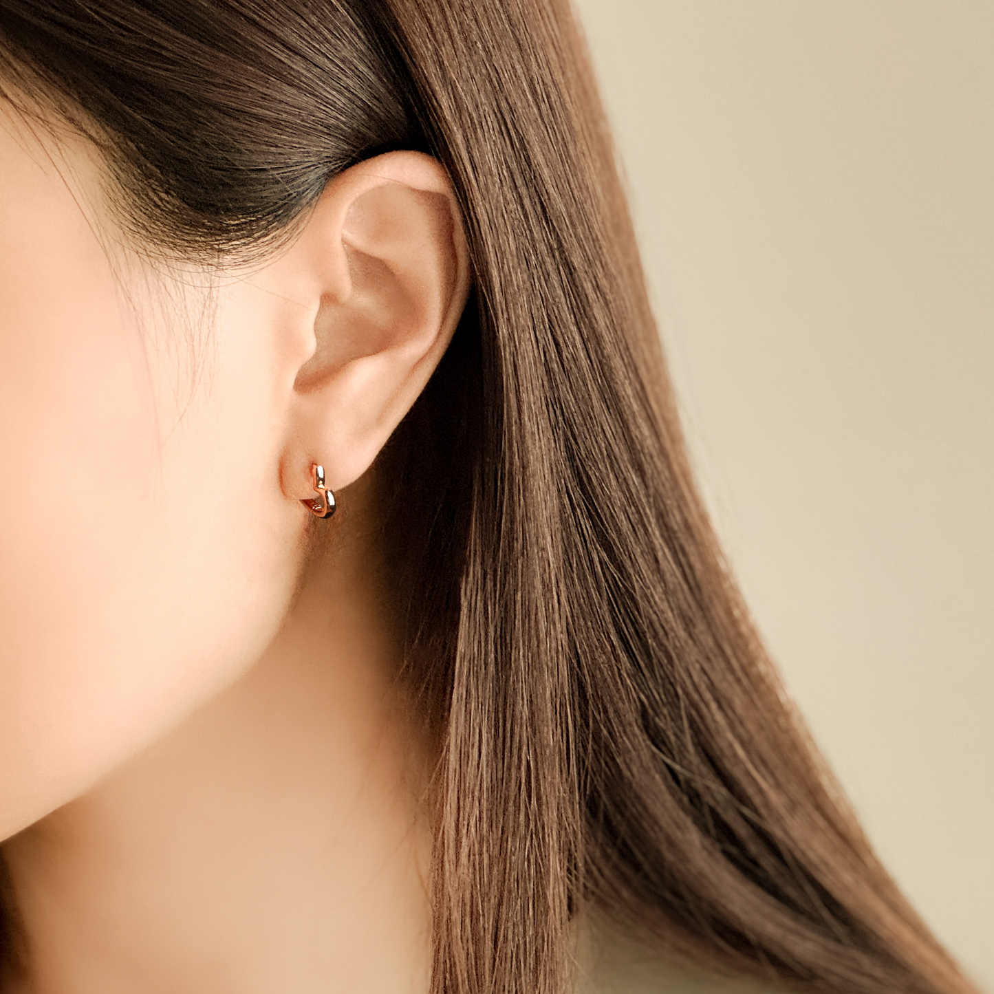 Close-up of an ear wearing a small earring with a neutral background