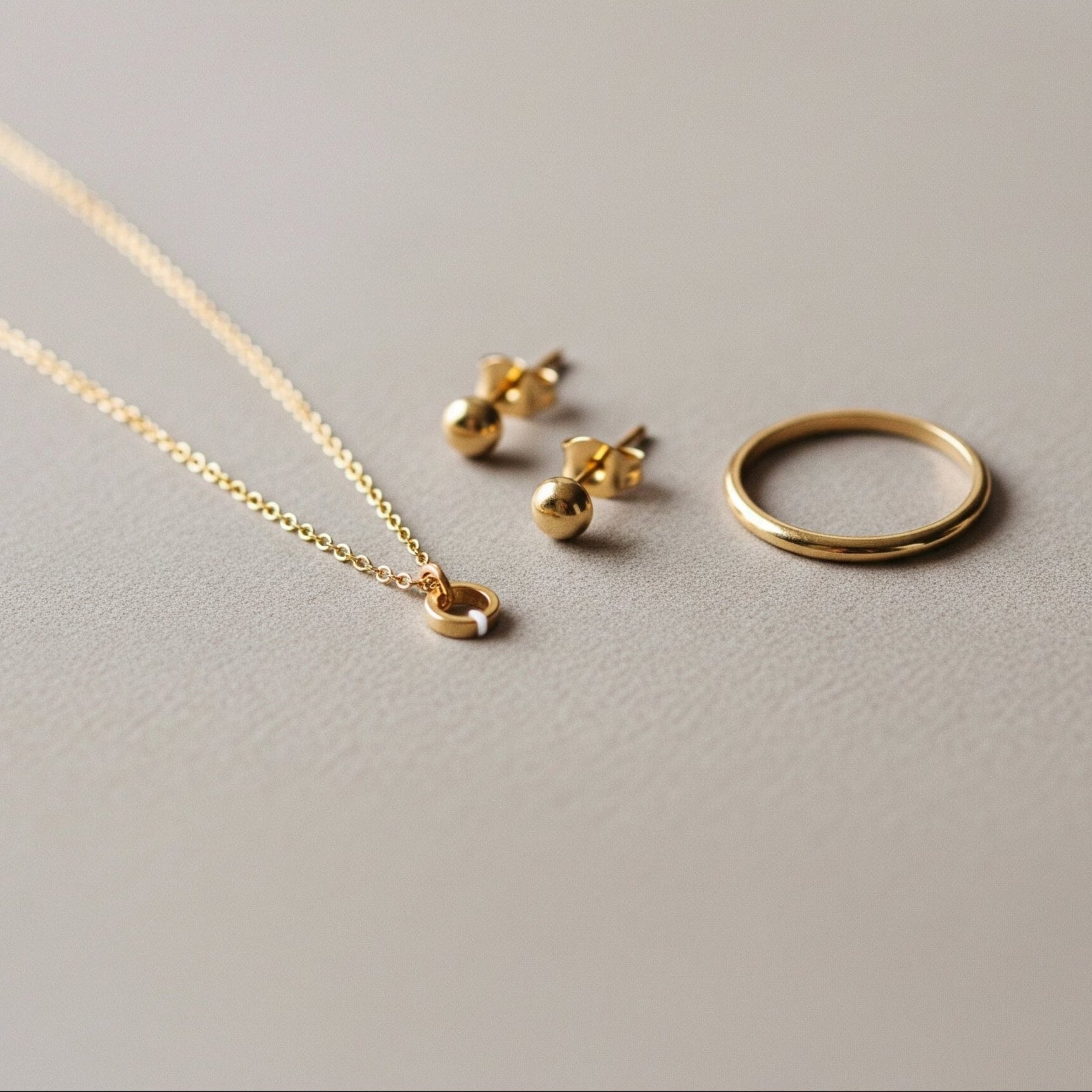 Gold necklace, earrings, and ring on a light gray background