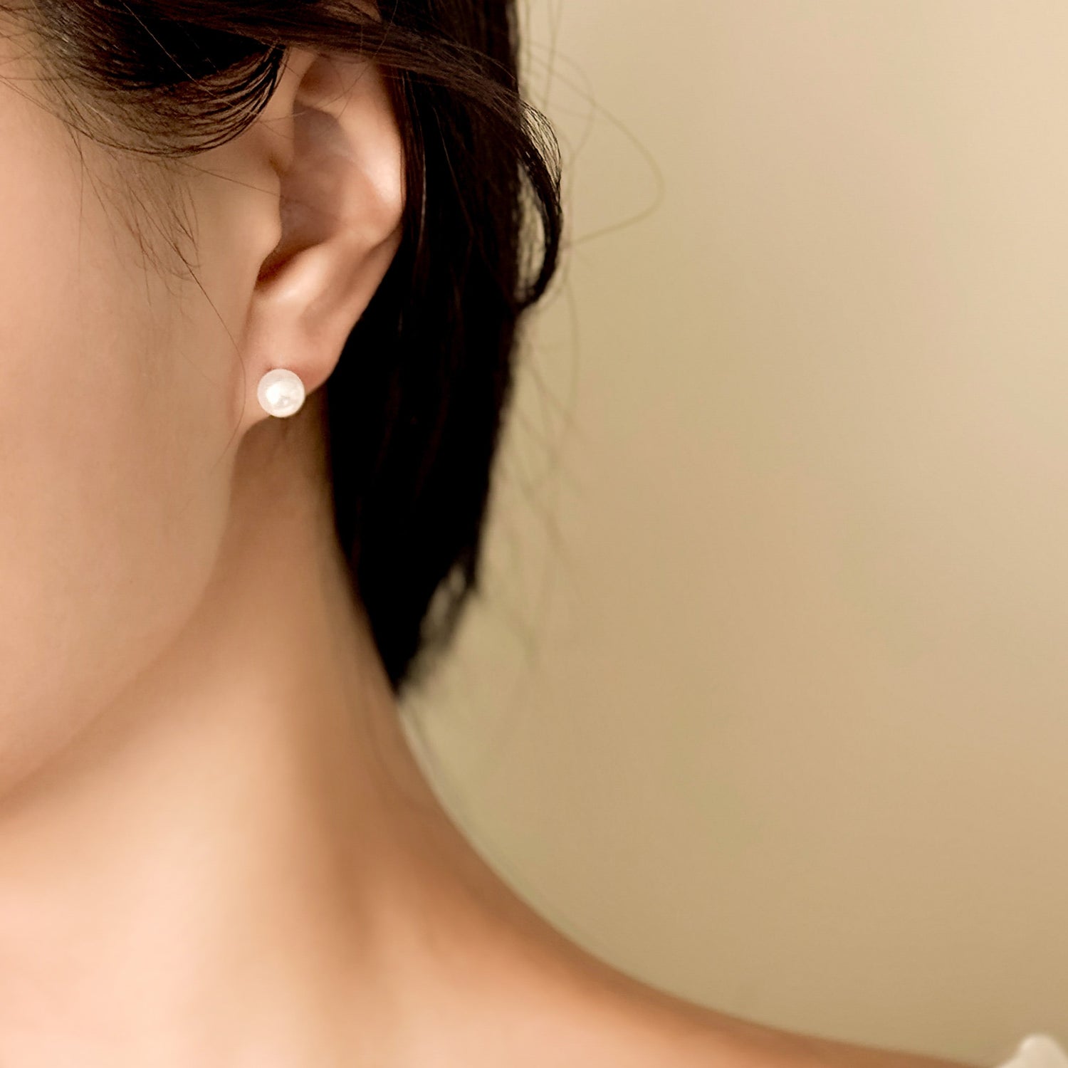 Close-up of an ear wearing a pearl earring with a neutral background