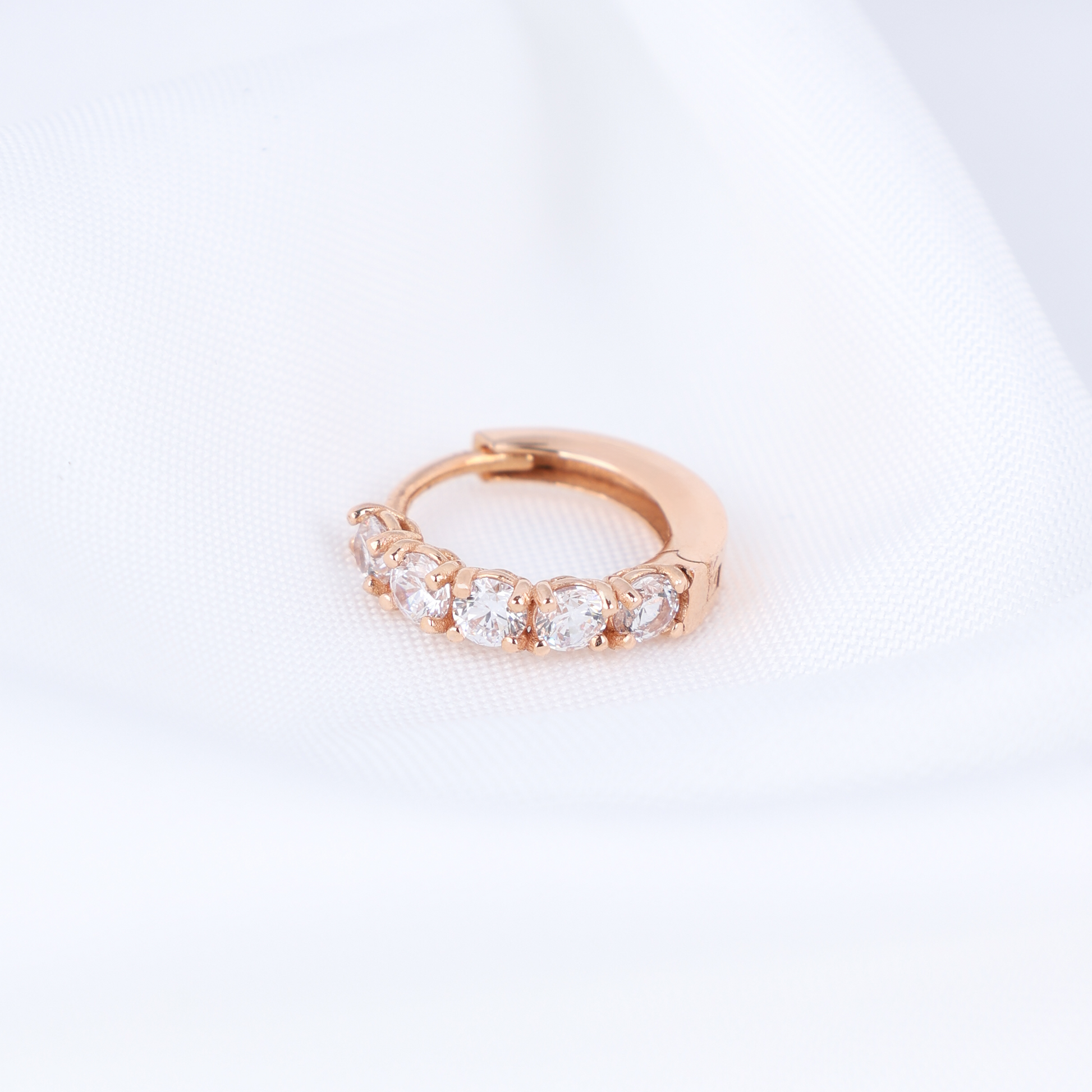 Rose gold huggie hoop earring with clear stones on a light gray background