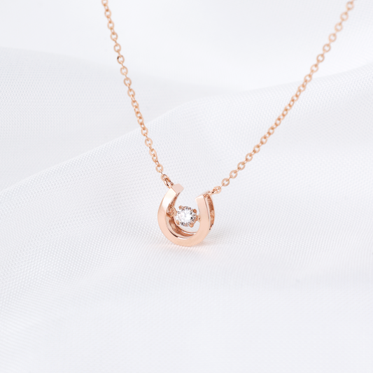 Rose gold horseshoe necklace with a diamond on a light gray background
