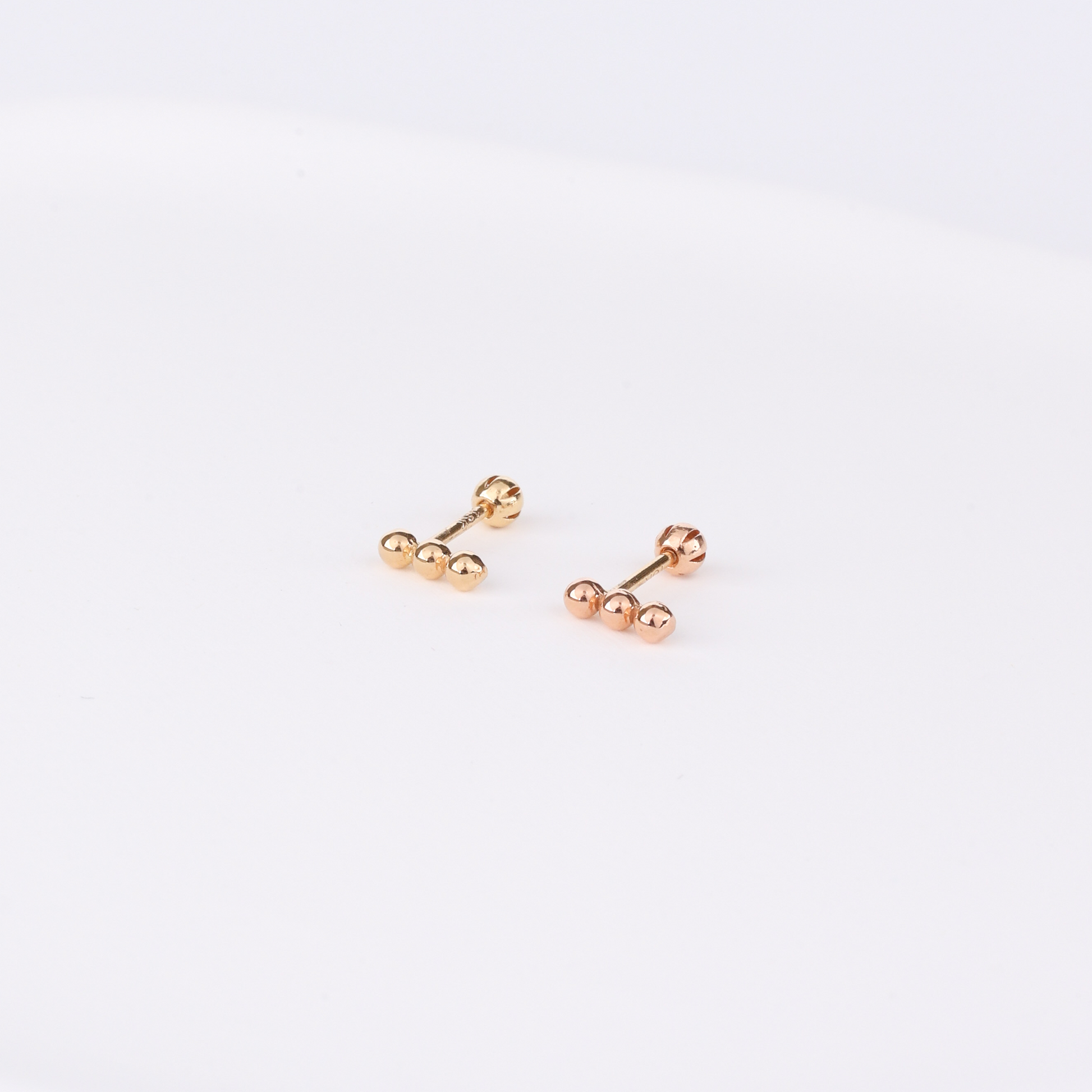 Two gold stud earrings in different finishes—yellow gold and rose gold—each featuring three horizontally aligned polished spheres with screw-back closures, displayed on a white background